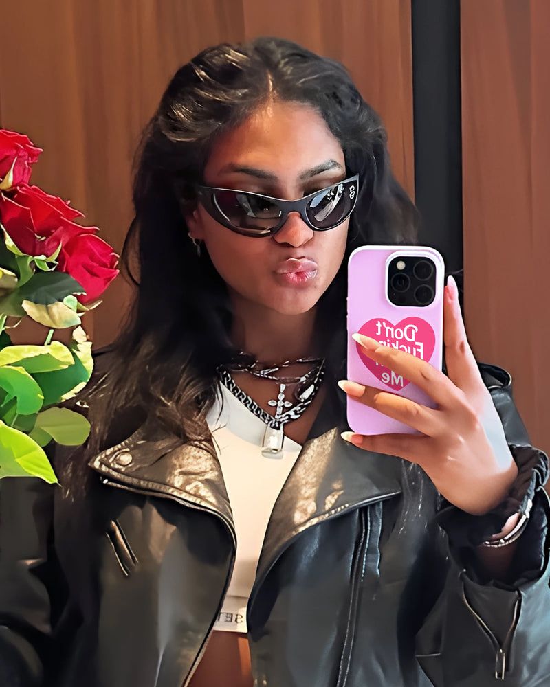 Woman in black leather jacket and sunglasses holding pink phone case with red rose
